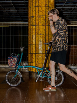 Brompton rider in front of a yellow industrial gate 